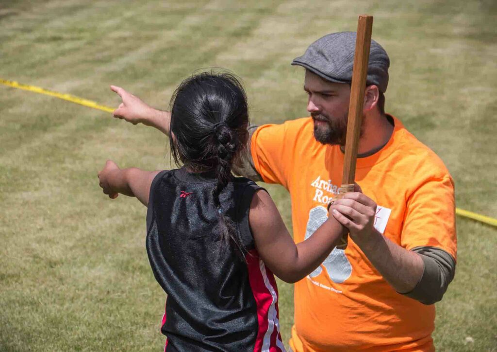 A volunteer helps a child at the Atlatl throwing activity at the 2017 Archaeology Roadshow in Harney County. Photo by Greg Shine