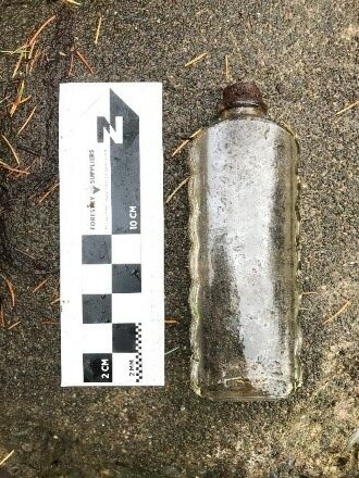 a historic glass bottle on the ground next to a scale and north arrow